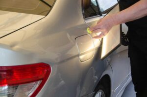 A close-up of a clean car door with a shallow dent being inspected under reflected light.