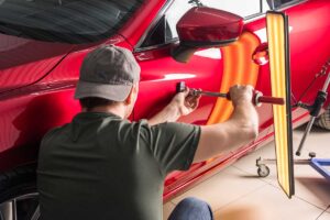 Technician carefully reshapes a shallow dent from behind a vehicle door using specialized hand tools.